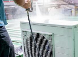 air conditioner cleaning by a man technician cleans condensing unit of air conditioner by spraying water air conditioner maintenance service at home or office worker working for ac mainten